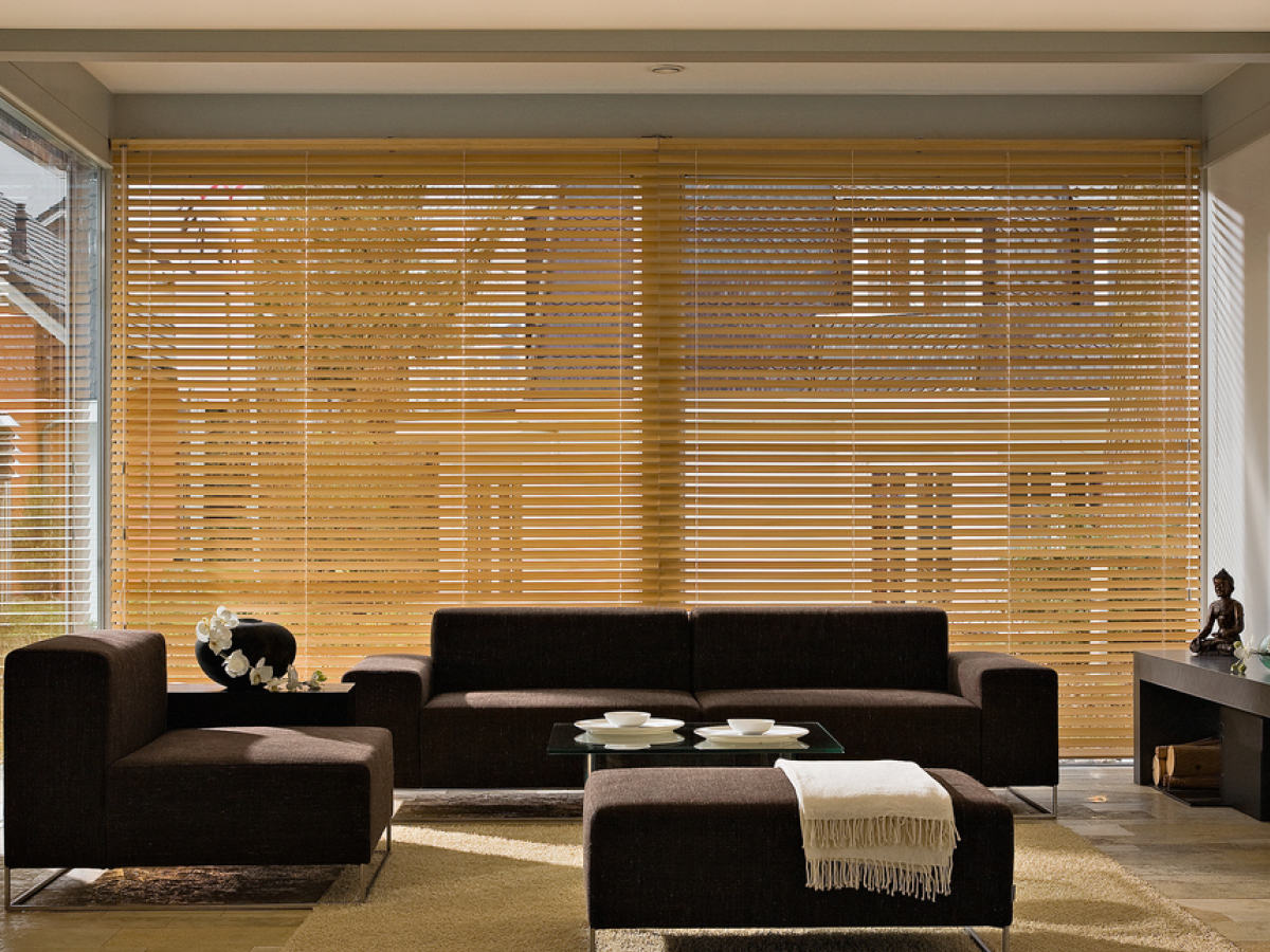 Eine hellbraune große Holzjalouse in einem Wohnzimmer.